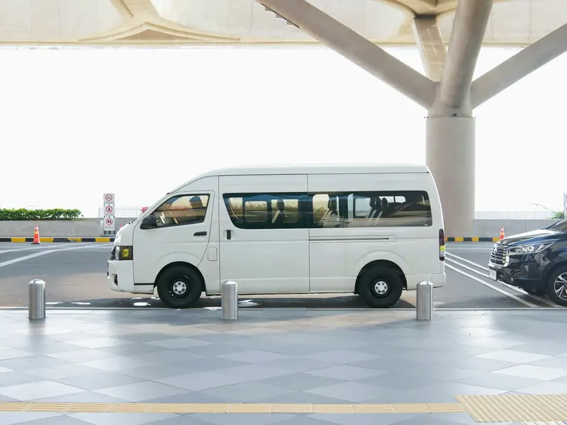 A white passenger van at an airport terminal drop-off